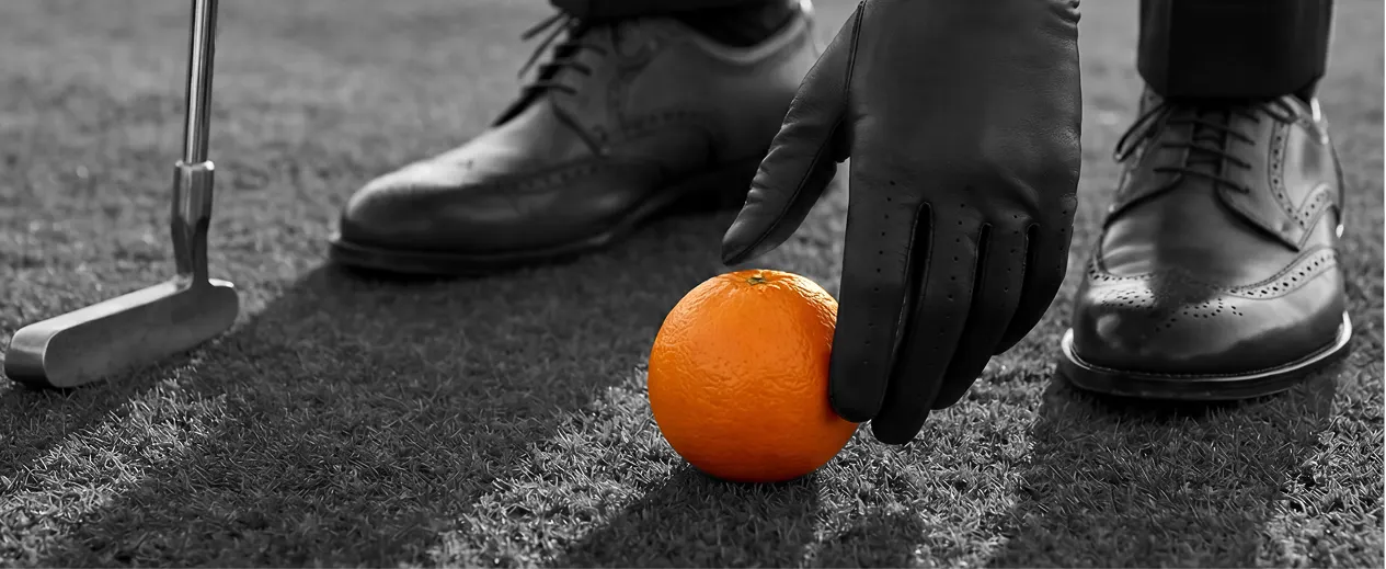 Black shoes, an orange and a golf club on grey surface — unconventional visual for corporate brand website